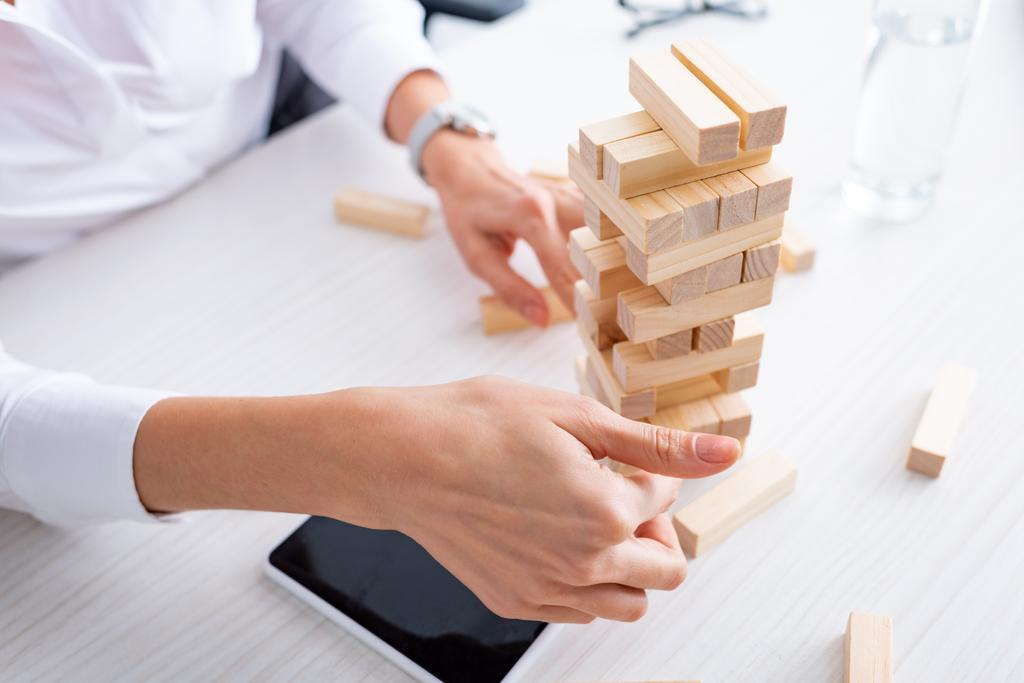 Oříznutý pohled na businesswoman hrát bloky dřeva věž hra v blízkosti smartphone u stolu  - Fotografie, Obrázek