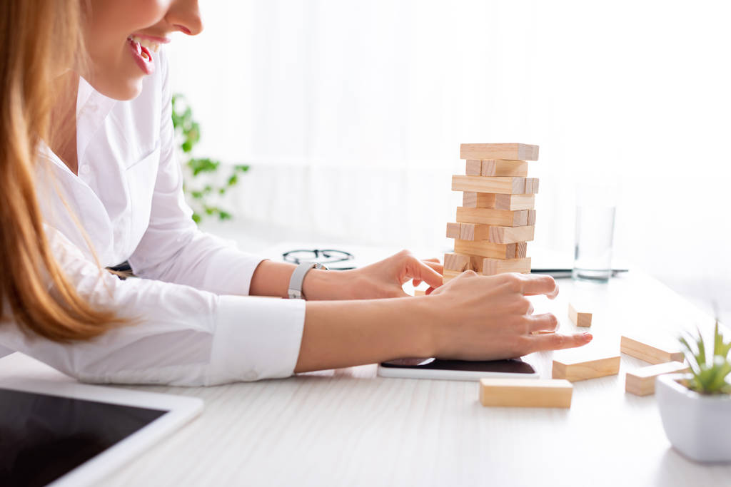 Cropped view of smiling businesswoman stacking wooden building blocks on table - Photo, Image