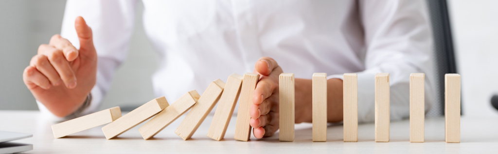Panoramic shot of businesswoman holding falling building blocks on table - Photo, Image