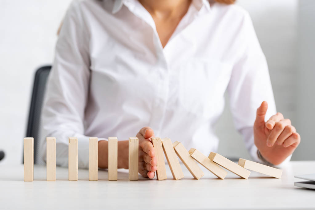 Selective focus of businesswoman holding falling building blocks on table  - 写真・画像