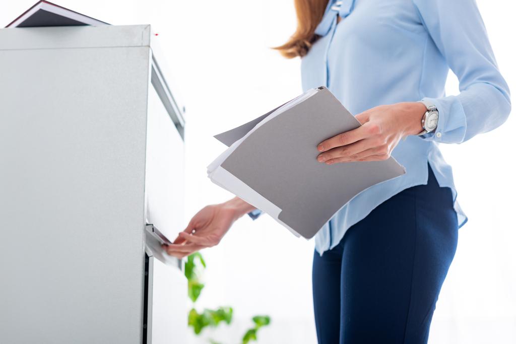 Cropped view of businesswoman holding paper folder and opening cabinet driver on white background - Fotoğraf, Görsel