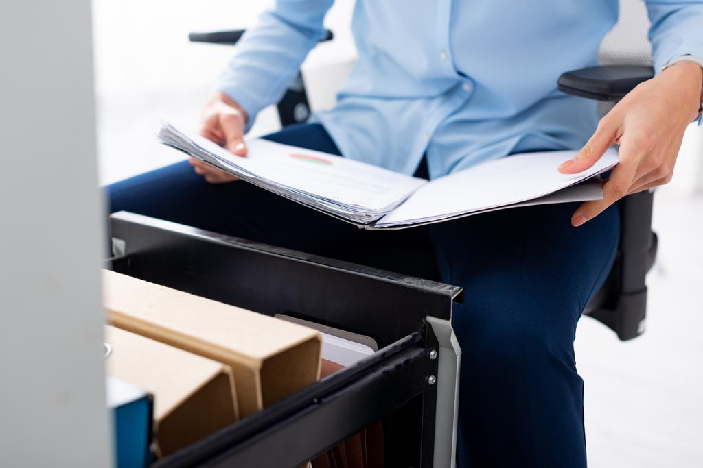 Cropped view of businesswoman holding folder with papers near open cabinet driver on white background - Photo, Image