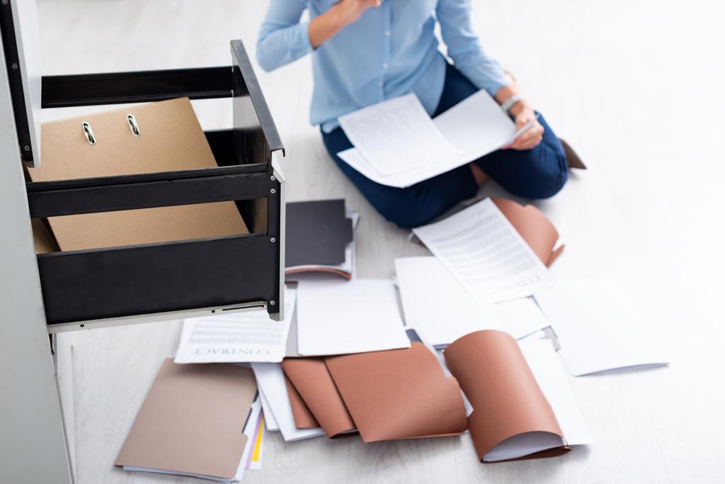 Ausgeschnittene Ansicht einer Geschäftsfrau mit Vertrag und Dokumenten in der Nähe eines offenen Schranktreibers auf dem Fußboden - Foto, Bild