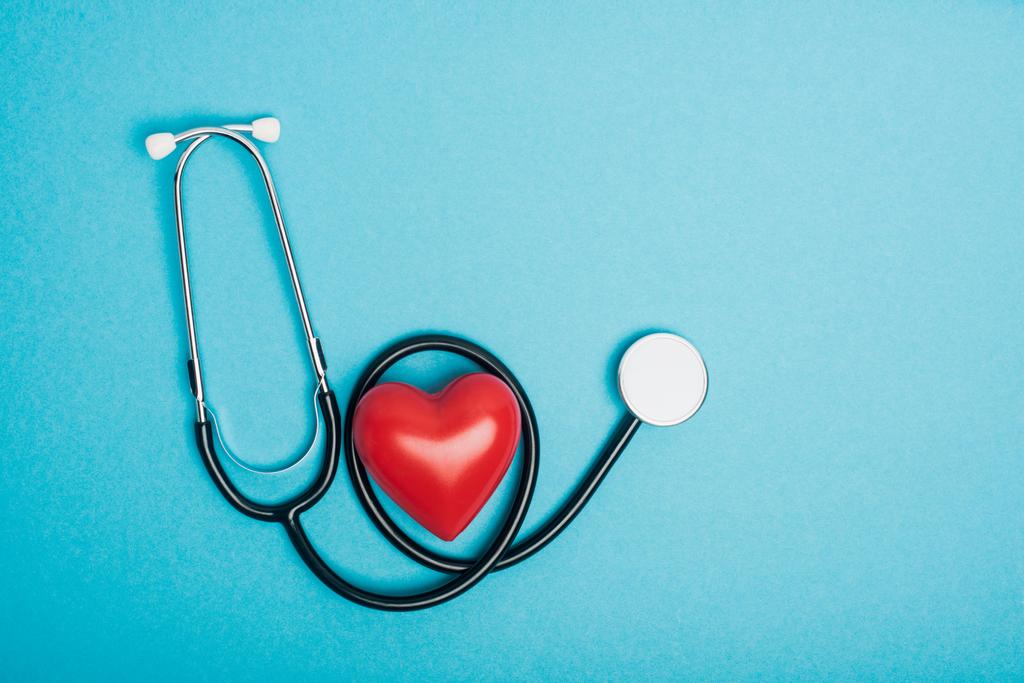 Draufsicht auf dekoratives rotes Herz mit Stethoskop auf blauem Hintergrund, Konzept zum Weltgesundheitstag - Foto, Bild