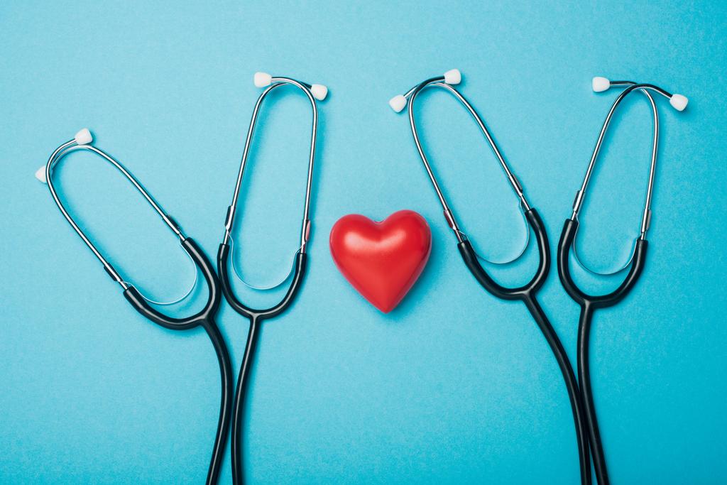 Κάτοψη της διακοσμητικής κόκκινης καρδιάς με στηθοσκόπια σε μπλε φόντο, έννοια παγκόσμια ημέρα υγείας - Φωτογραφία, εικόνα