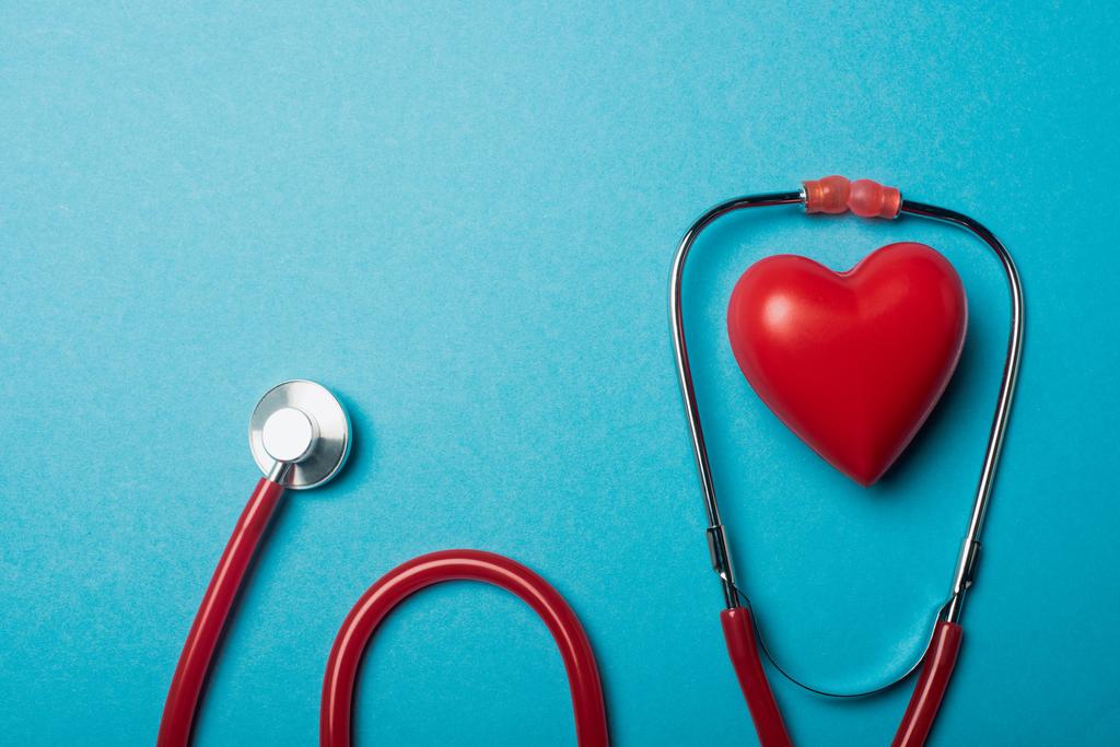Bovenaanzicht van rode hart en stethoscoop op blauwe achtergrond, wereld gezondheidsdag concept - Foto, afbeelding