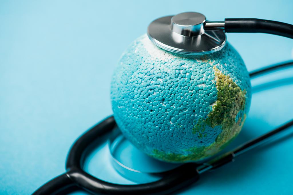 Selective focus of black stethoscope connected with globe on blue background, world health day concept - Photo, Image