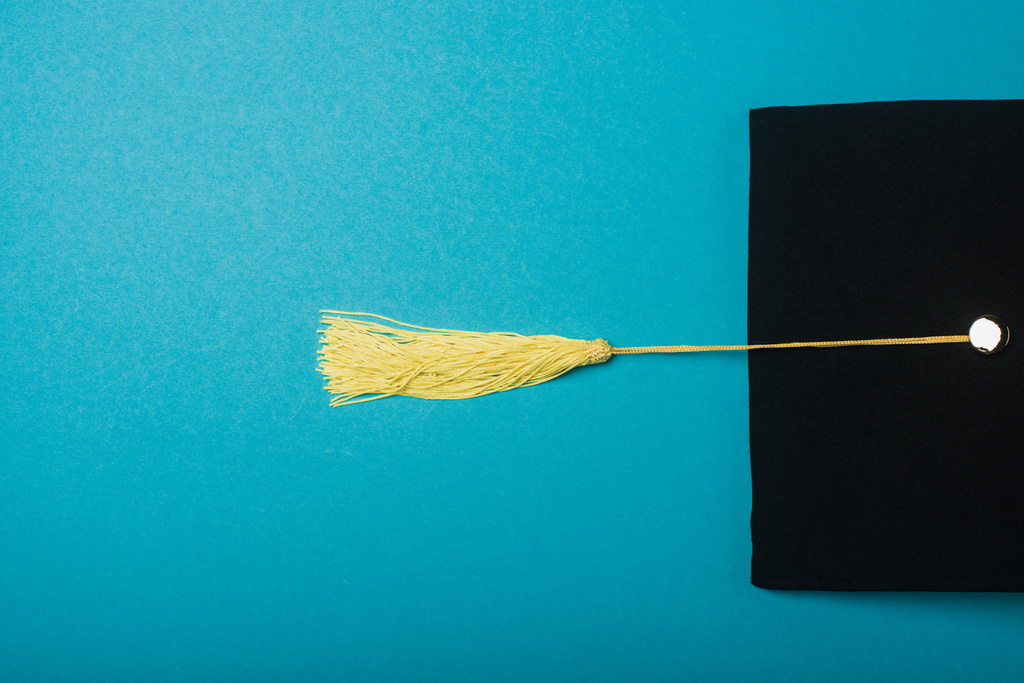 Κάτοψη του μαύρου καπέλου αποφοίτησης με κίτρινη φούντα σε μπλε φόντο - Φωτογραφία, εικόνα