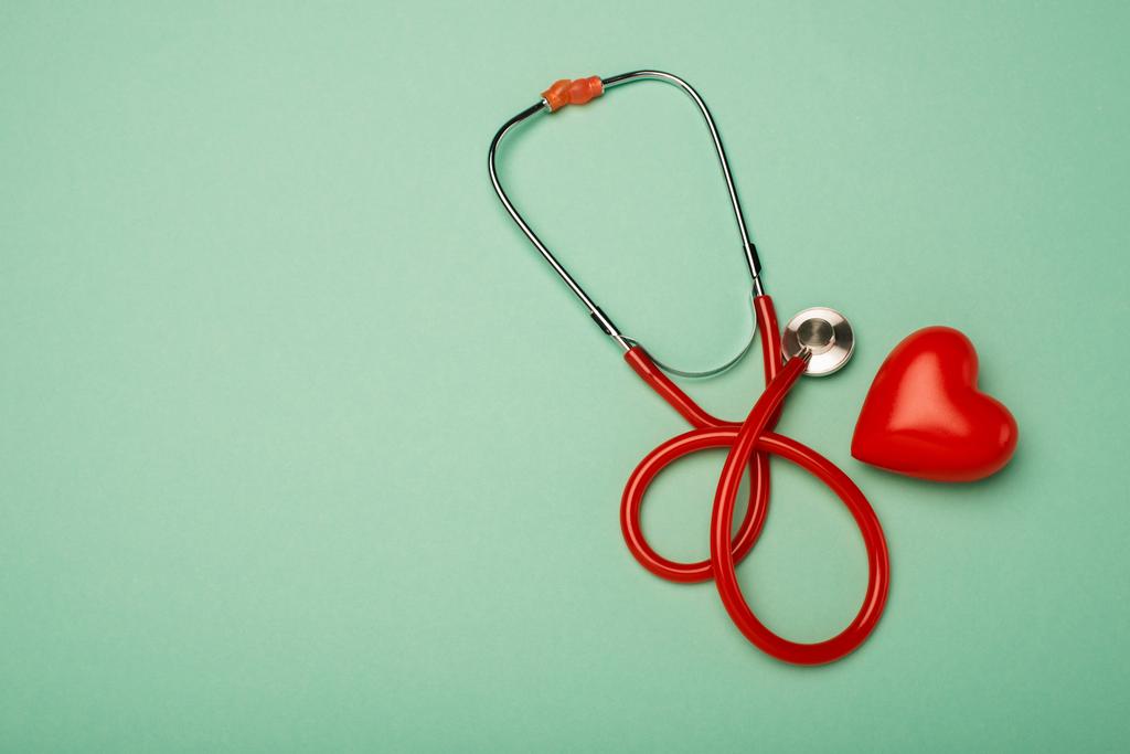 Κάτοψη του στηθοσκοπίου δίπλα στην κόκκινη καρδιά σε πράσινο φόντο, έννοια παγκόσμια ημέρα υγείας - Φωτογραφία, εικόνα