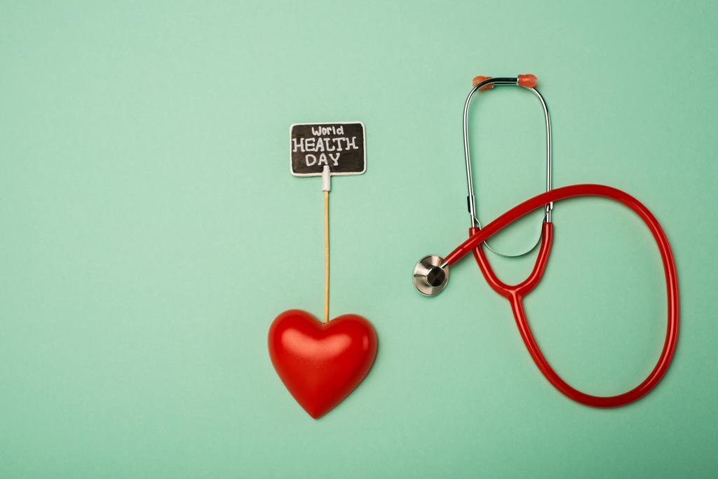 Horní pohled na stetoskop, dekorativní srdce a kartu se světovým zdravím den nápisy na zeleném pozadí - Fotografie, Obrázek