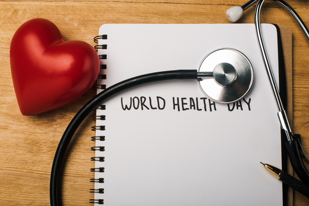 Dekoratif kalp manzarası, steteskop, defter üzerine kalem ve tahta arka planda Dünya Sağlık Günü yazıları. - Fotoğraf, Görsel