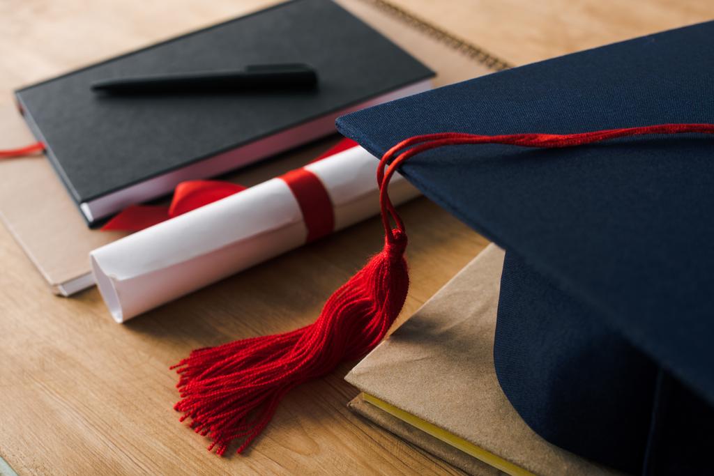 Selective focus of notebooks with pen, diploma and graduation cap on wooden background - Photo, Image