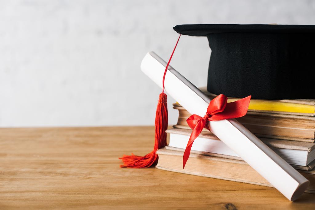 Diploma con bellissimo fiocco e cappuccio di laurea con nappa rossa in cima a libri sul tavolo su sfondo bianco
 - Foto, immagini