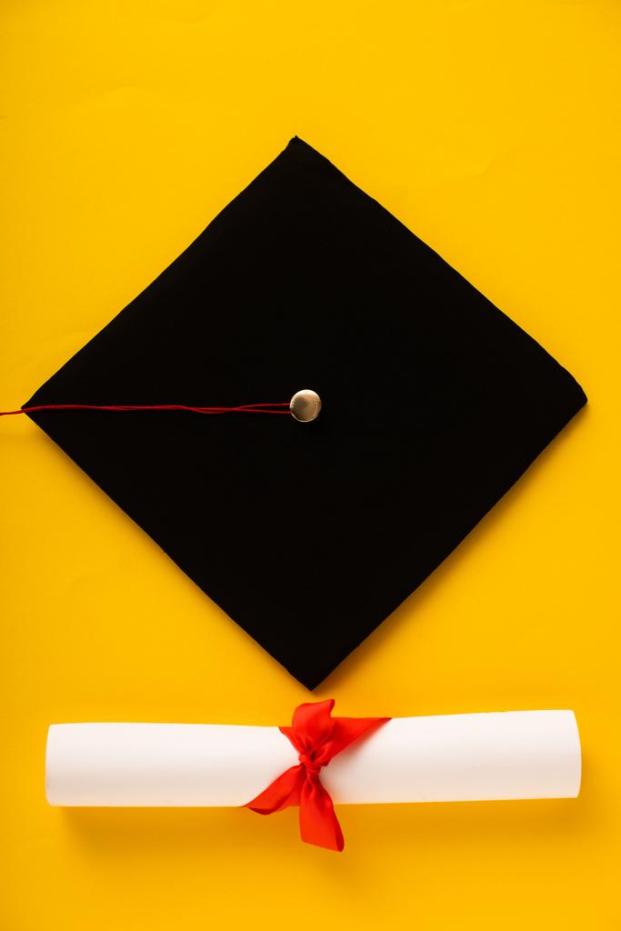 Widok z góry dyplom z pięknym łukiem i czarnym podziałką czapki na żółtym tle - Zdjęcie, obraz
