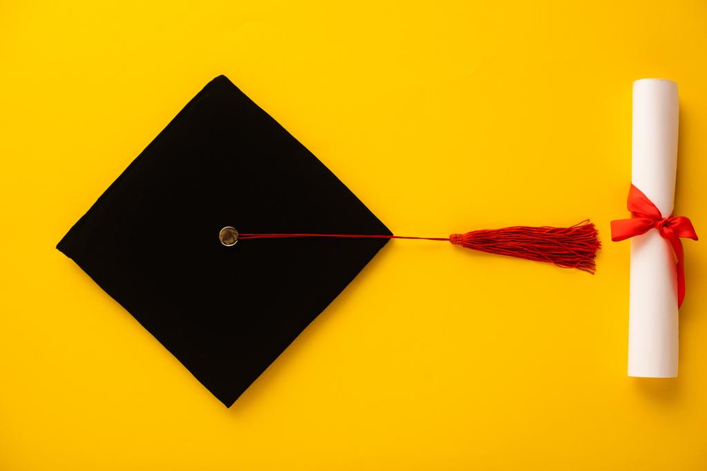 Diplom und Abschlussmütze von oben mit roter Quaste auf gelbem Hintergrund - Foto, Bild