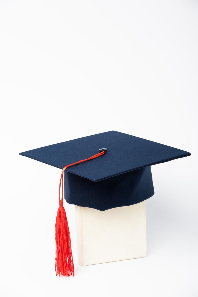 Gorra de graduación azul con borla roja en libro sobre fondo blanco
 - Foto, imagen