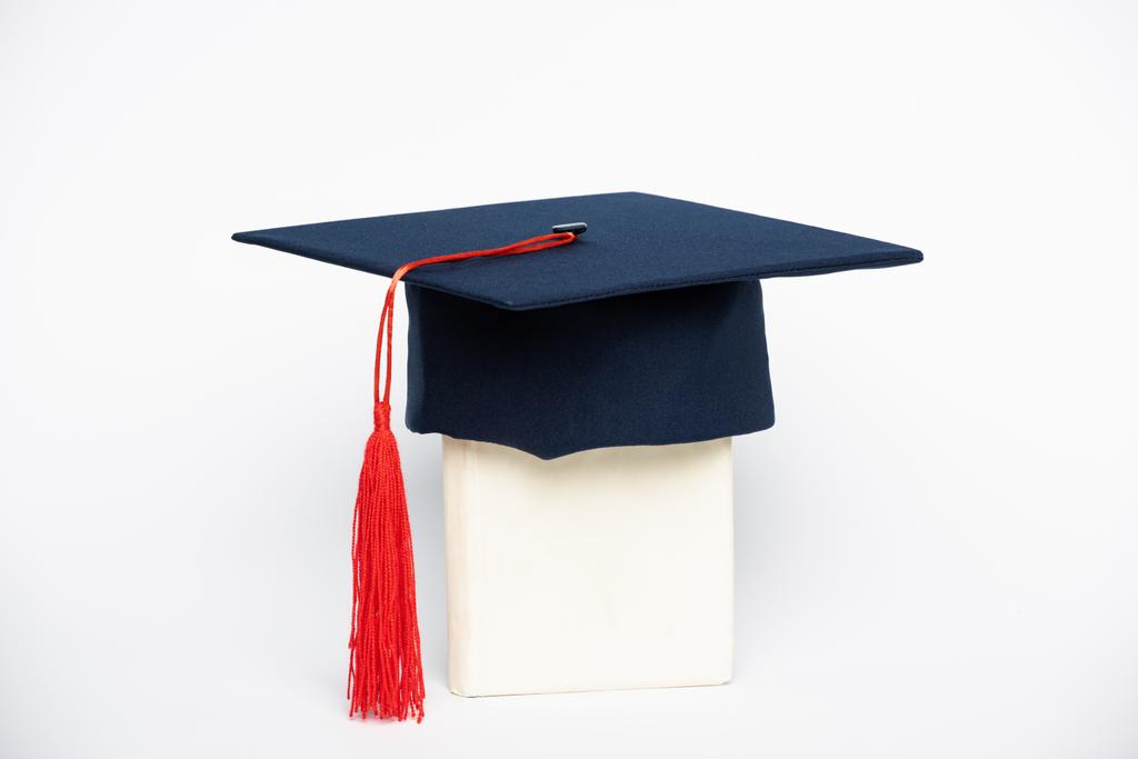 Graduation cap met rode kwastje op boek op witte achtergrond - Foto, afbeelding