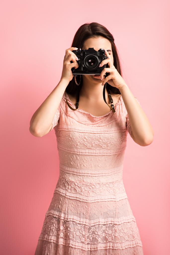 φωτογράφος σε κομψό φόρεμα λήψη φωτογραφιών σε ψηφιακή φωτογραφική μηχανή σε ροζ φόντο - Φωτογραφία, εικόνα