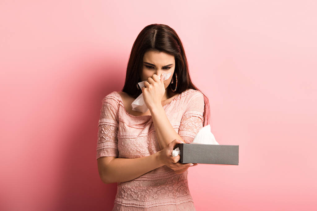 ziek meisje vegen neus met papier servet op roze achtergrond - Foto, afbeelding