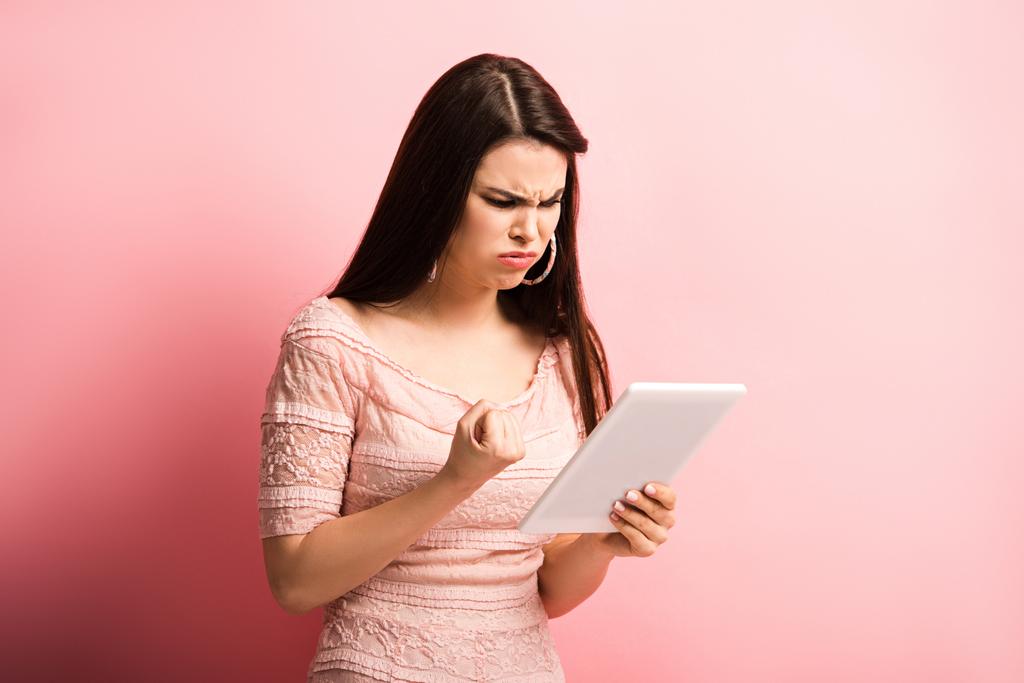 chica enojada mostrando puño cerrado durante el chat de vídeo en la tableta digital sobre fondo rosa
 - Foto, imagen