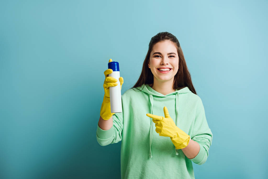 happy housewife pointing with finger at air freshener on blue background - Photo, Image