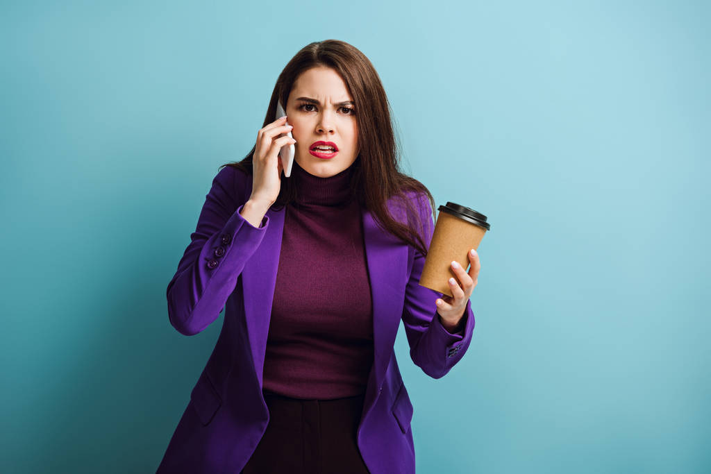 сердитая девушка разговаривает по смартфону и держит кофе на синем фоне
 - Фото, изображение