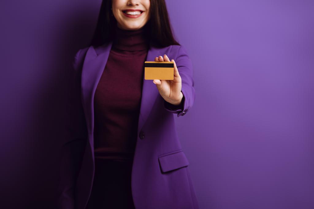 περικοπή άποψη του χαμογελαστού γυναίκα δείχνει πιστωτική κάρτα σε μωβ φόντο - Φωτογραφία, εικόνα