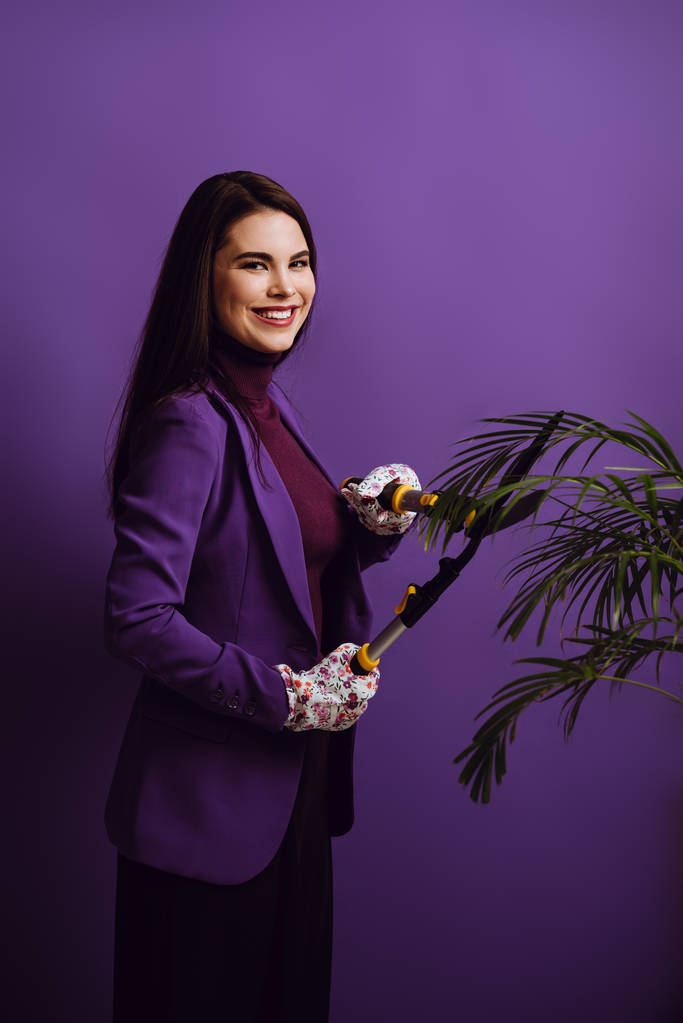 gelukkig jong vrouw snijden plant met tuinieren schaar op paarse achtergrond - Foto, afbeelding
