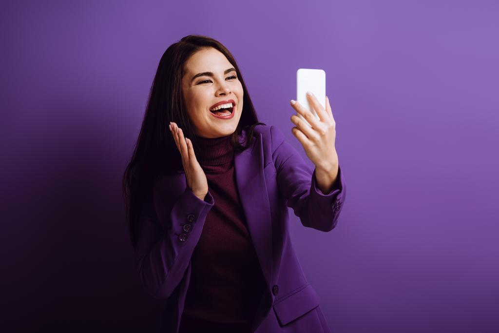 happy girl waving hand while having video call on purple background - Photo, Image