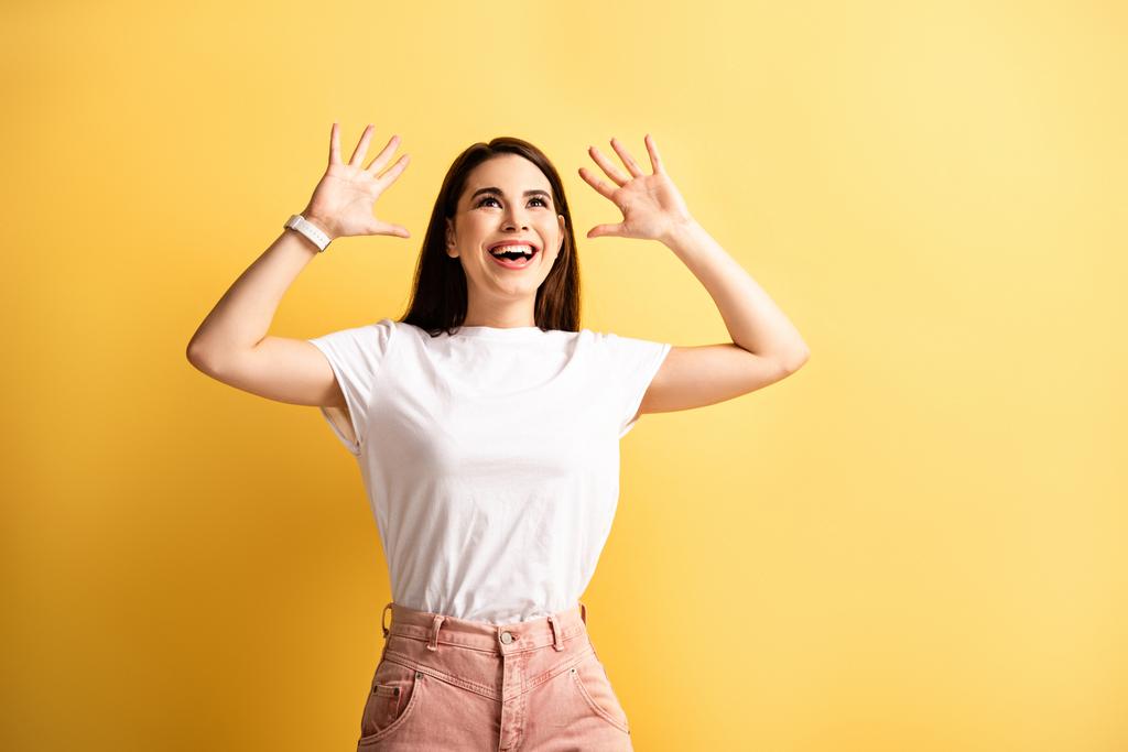 szczęśliwy dziewczyna pokazując wow gest podczas patrząc w górę na żółtym tle - Zdjęcie, obraz