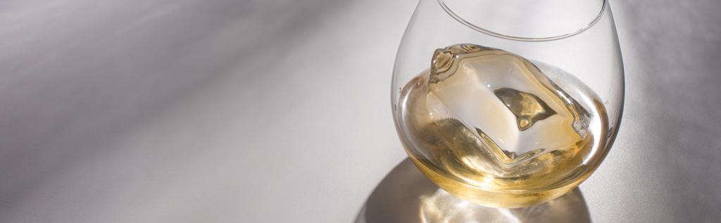 průhledné sklo s kostkou ledu a whisky na bílém stole se stínem, panoramatický výstřel - Fotografie, Obrázek