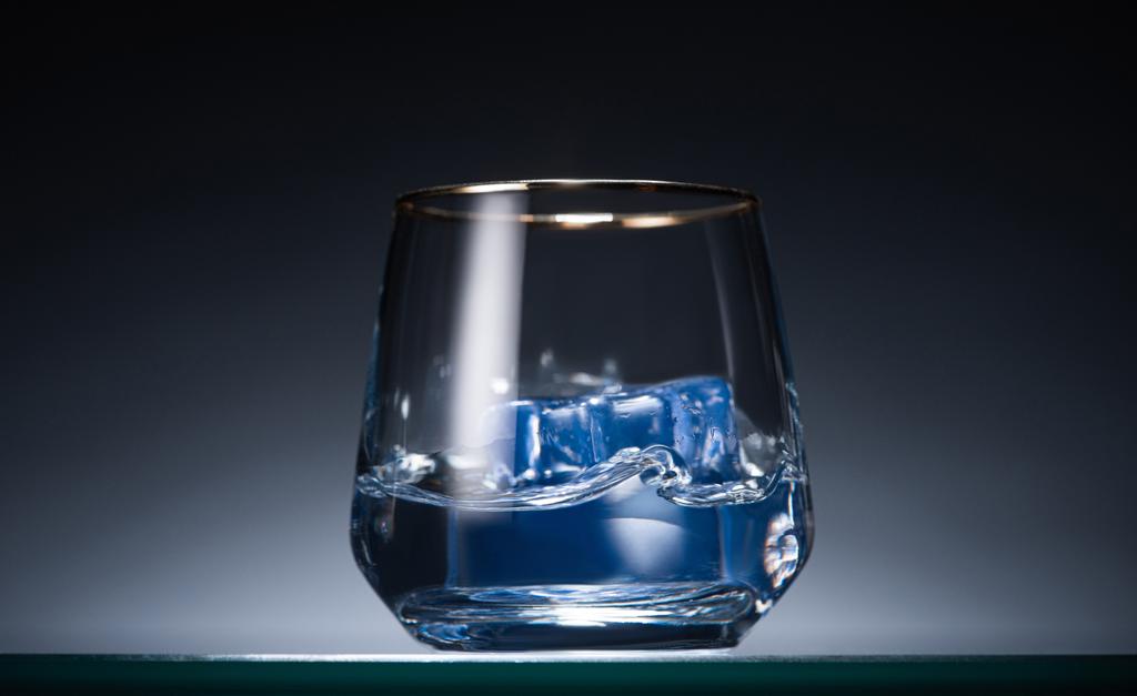 vidrio transparente con cubitos de hielo y vodka en oscuro con luz de fondo azul
 - Foto, imagen