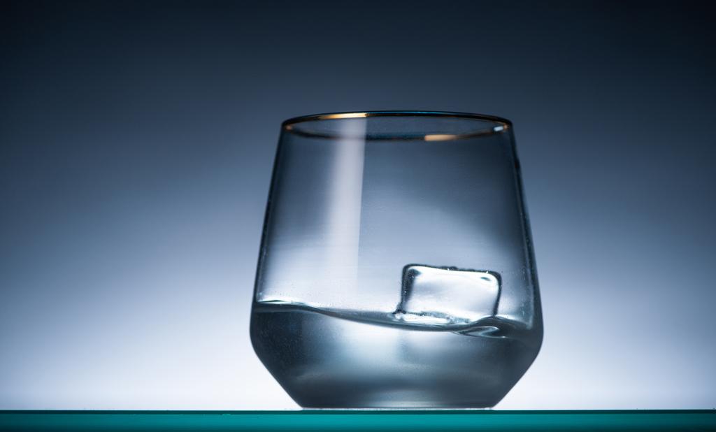 vidrio transparente con cubo de hielo y vodka en la oscuridad con luz de fondo
 - Foto, Imagen