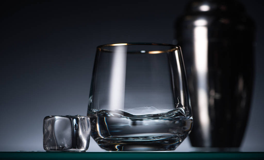 селективный фокус прозрачного стекла с водкой рядом со льдом в темноте с задним светом и шейкером
 - Фото, изображение