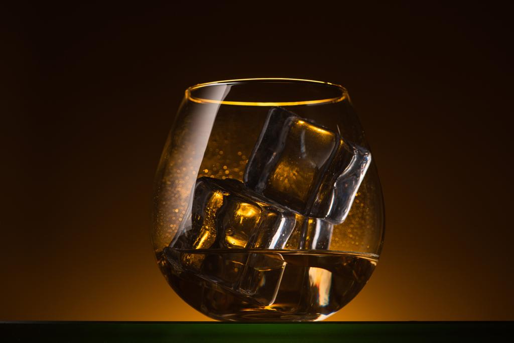 vidrio transparente con cubitos de hielo y vodka en la oscuridad con luz de fondo caliente
 - Foto, imagen