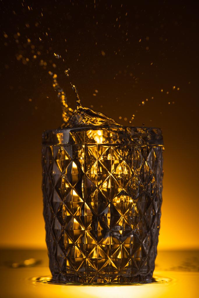 facettiertes Glas mit spritzendem Wodka im Dunkeln mit warmem Gegenlicht - Foto, Bild