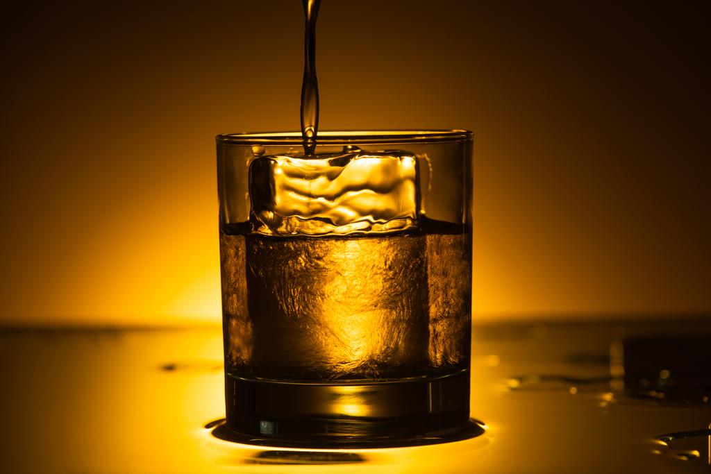 vodka verter en vidrio transparente con cubo de hielo en la oscuridad con luz de fondo caliente
 - Foto, imagen
