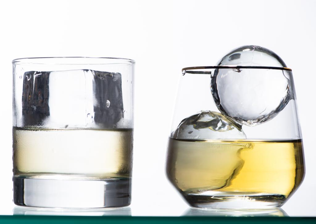 przezroczyste szklanki ze złotym płynem i lodem izolowane na biało - Zdjęcie, obraz