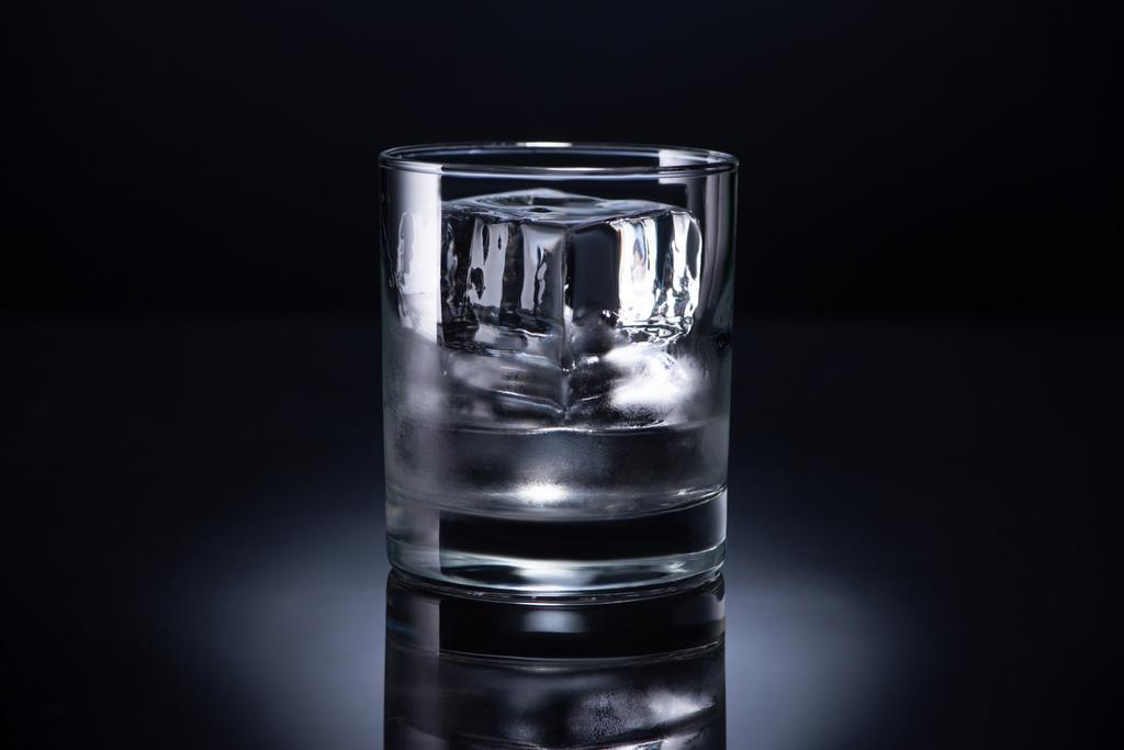 transparant glas met ijsblokje en wodka op zwarte achtergrond - Foto, afbeelding