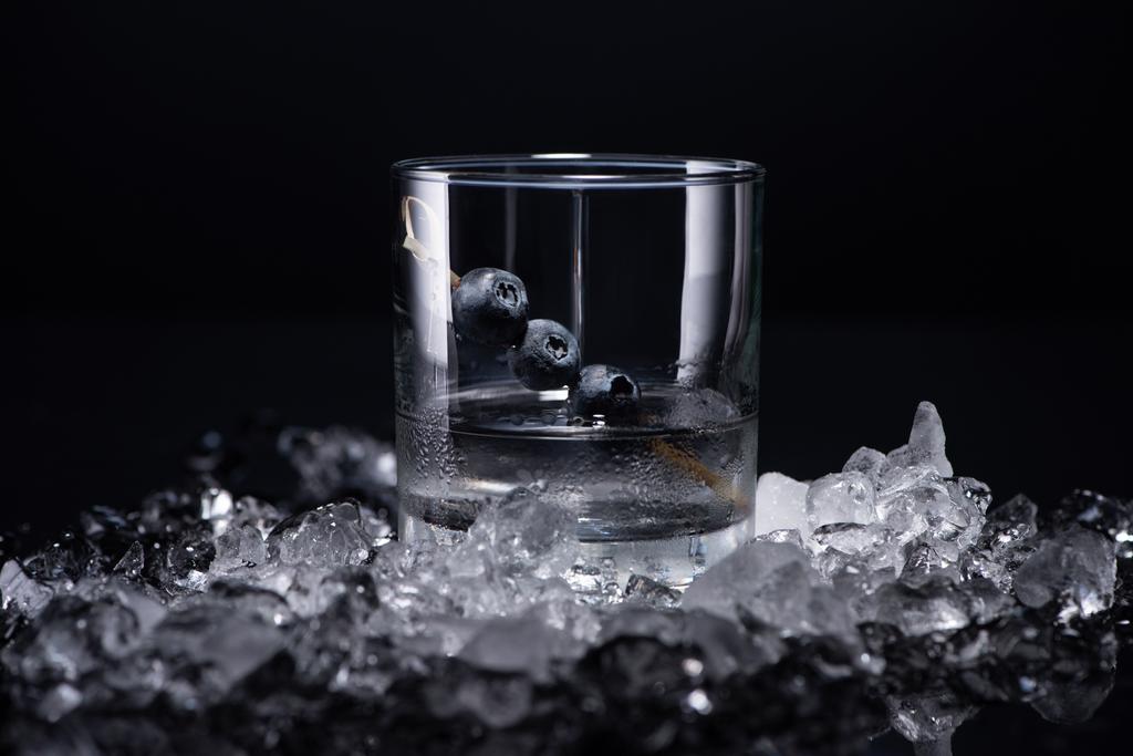 átlátszó üveg vodka és áfonya közelében zúzott jég elszigetelt fekete - Fotó, kép