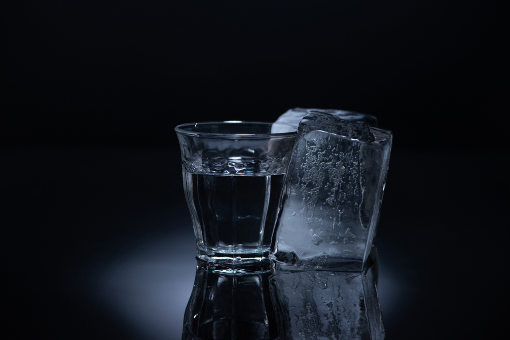 transparant glas met ijsblokje en wodka op zwarte achtergrond - Foto, afbeelding