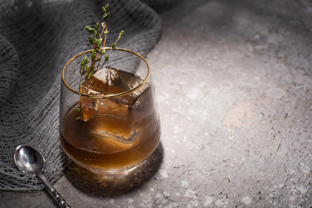 vidrio transparente con hierba, cubo de hielo y whisky en la superficie de hormigón con tela de malla y cuchara
 - Foto, imagen