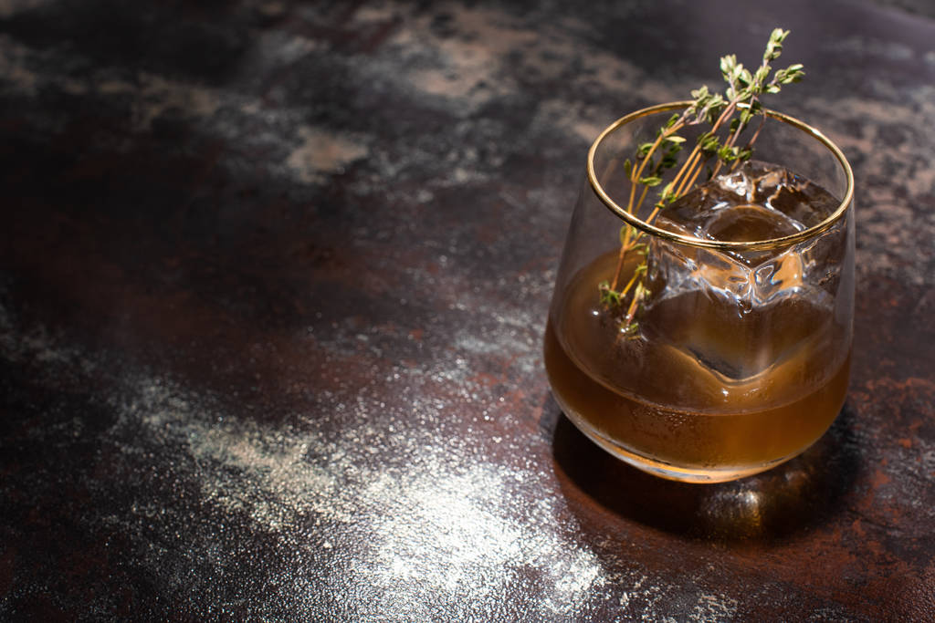 transparent glass with herb, ice cube and whiskey on weathered surface - Photo, Image