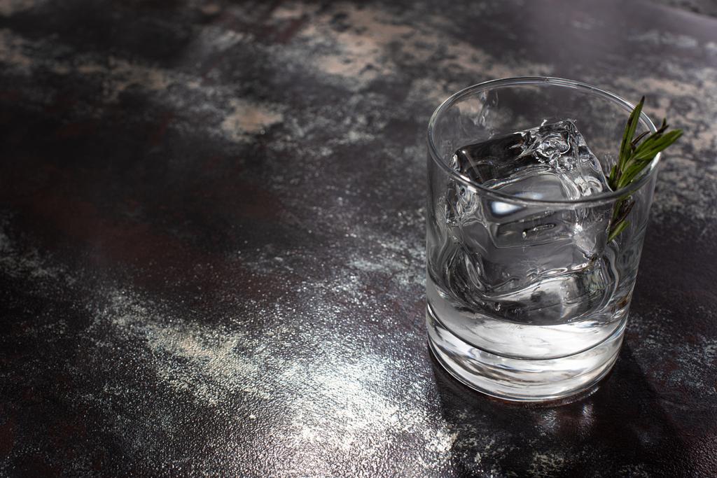 átlátszó üveg rozmaringgal, jégkockával és vodkával időjárással átitatott felületen - Fotó, kép