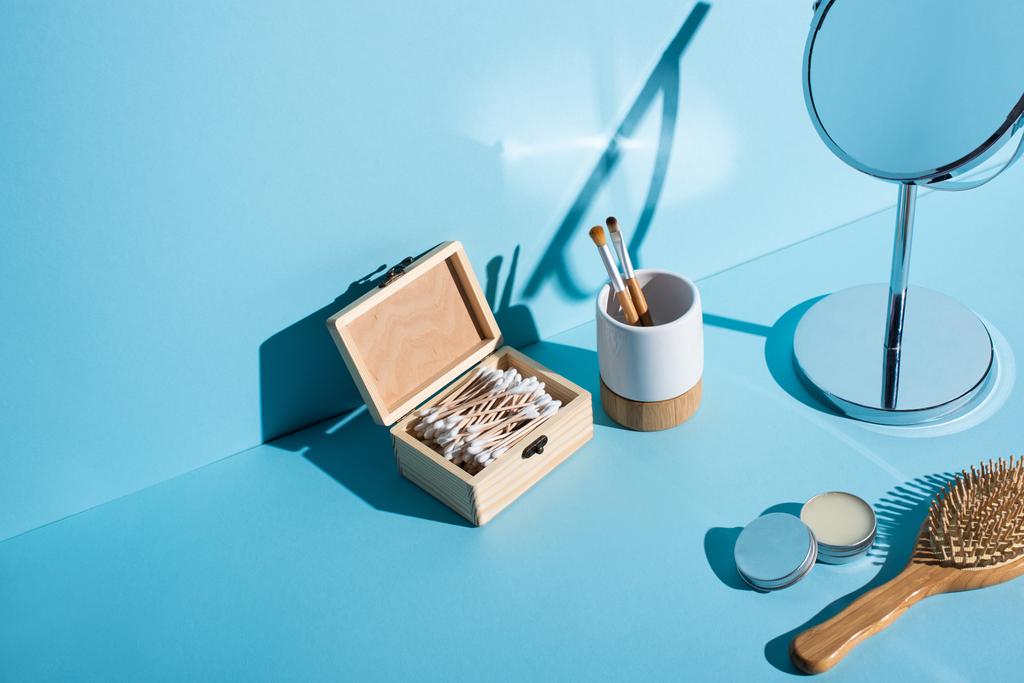 化粧ブラシ付き歯ブラシホルダー、耳スティックの箱、ミラー、青の背景にワックスとヘアブラシの瓶、ゼロ廃棄物の概念 - 写真・画像