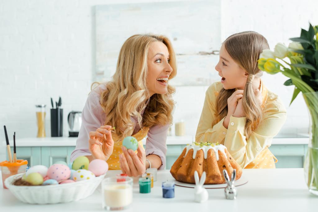 gelukkig geld en dochter kijken elkaar aan bij paastaart, kippeneieren, decoratieve konijnen en tulpen  - Foto, afbeelding