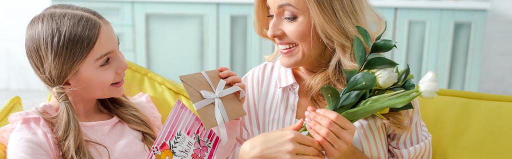 панорамний знімок веселого хлопчика, що тримає подарунки та вітальні листівки з днем щасливих матерів, що розпускається біля матері
  - Фото, зображення