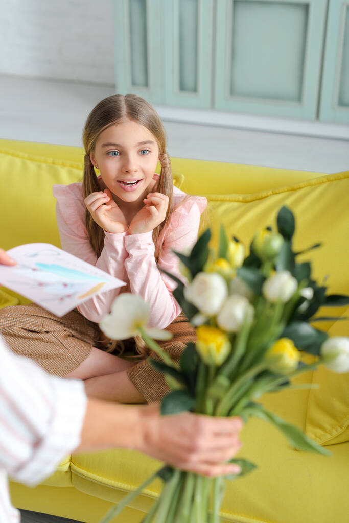 enfoque selectivo del niño sorprendido mirando las flores en la mano de la madre
  - Foto, Imagen