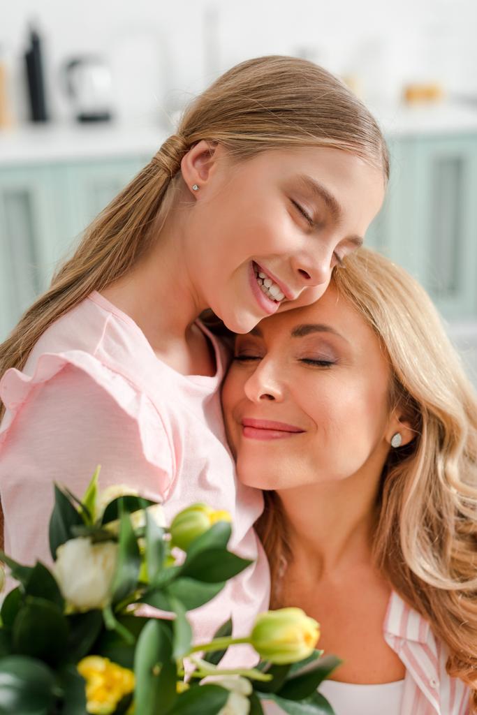 selective focus of happy mother and daughter smiling near tulips  - Fotoğraf, Görsel