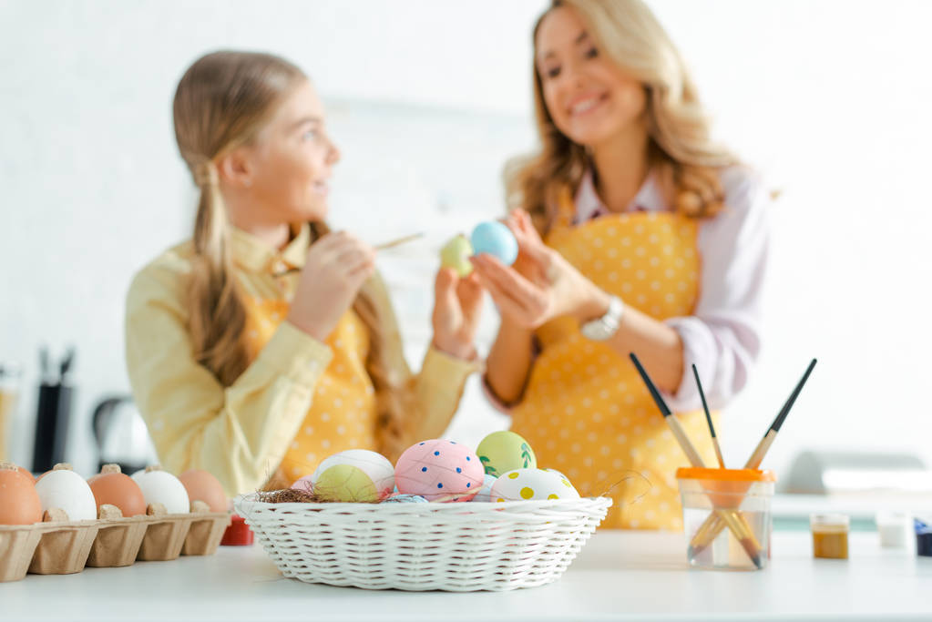 foyer sélectif de panier avec des œufs de Pâques peints près de mère heureuse et fille
  - Photo, image